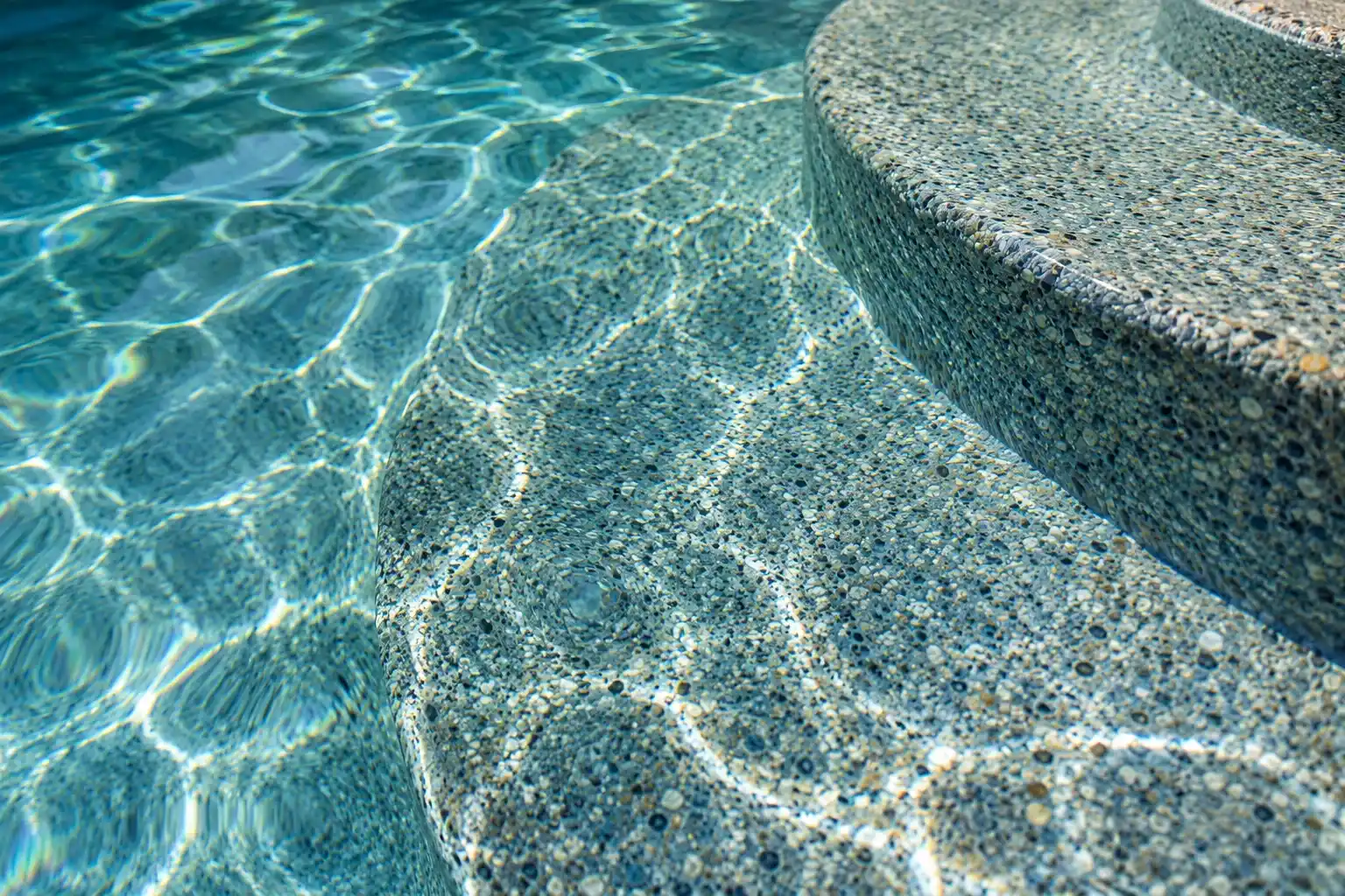 Close view of a blue gray pebble finish under clear pool water