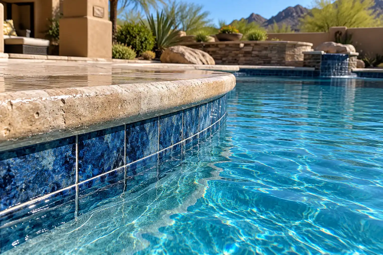 Deep blue waterline tile under travertine coping at the edge of a pool